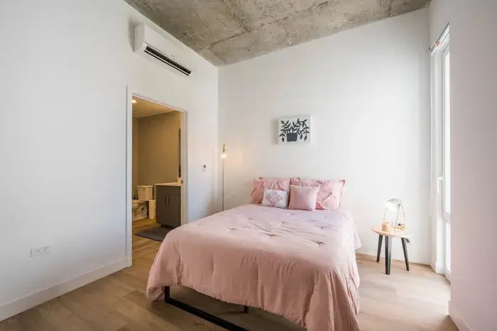 Modern bedroom featuring a pink bedspread, decorative pillows, and minimalist decor at Post Chicago Apartments, Lincoln Park furnished apartments.