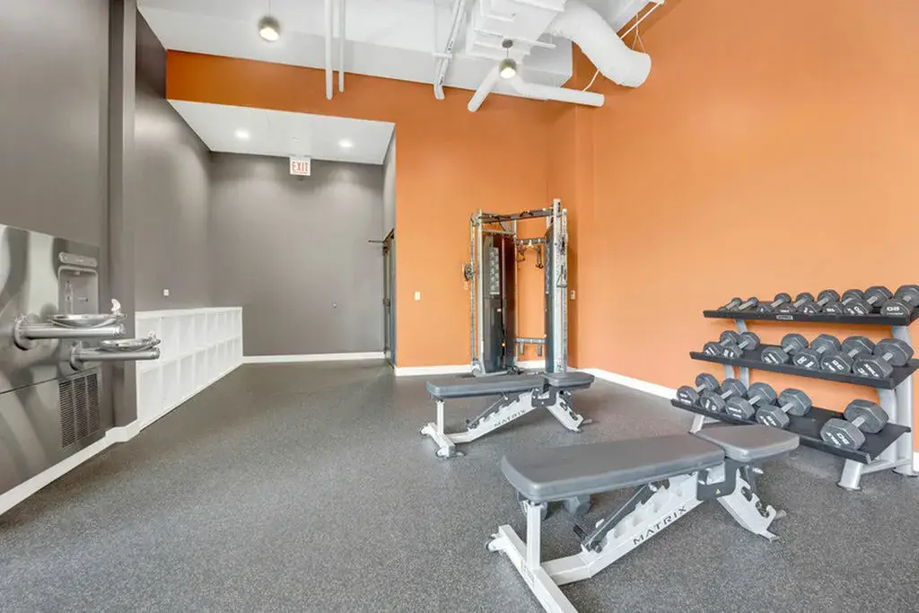 Modern gym interior featuring weight benches, a cable machine, and a rack of dumbbells at Post Chicago Apartments - Co-living apartments in Chicago