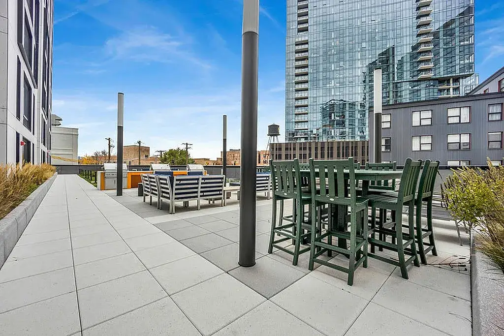 Rooftop terrace with green outdoor furniture, featuring a dining area and grill stations at Post Chicago Apartments - Co-living apartments in Chicago
