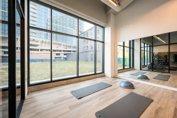 Modern fitness studio with large windows, featuring exercise mats and a balance trainer, overlooking a construction site and green space at Post Chicago Apartments - Furnished apartments for rent Chicago