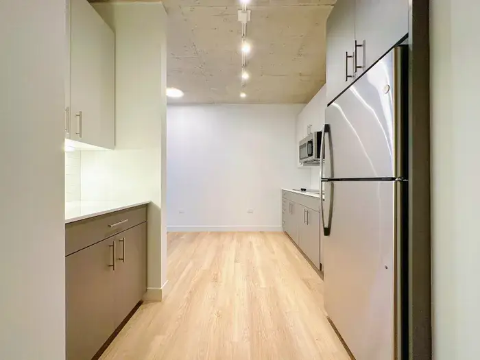 Modern kitchen interior featuring stainless steel appliances, including a refrigerator and microwave, with sleek cabinetry and warm wood flooring at Post Chicago Apartments.