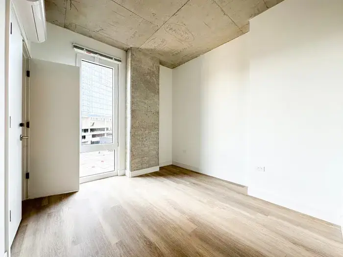 Modern apartment interior featuring a spacious room with hardwood flooring, large window, and concrete accent wall at Post Chicago Apartments, Lincoln Park furnished apartments.